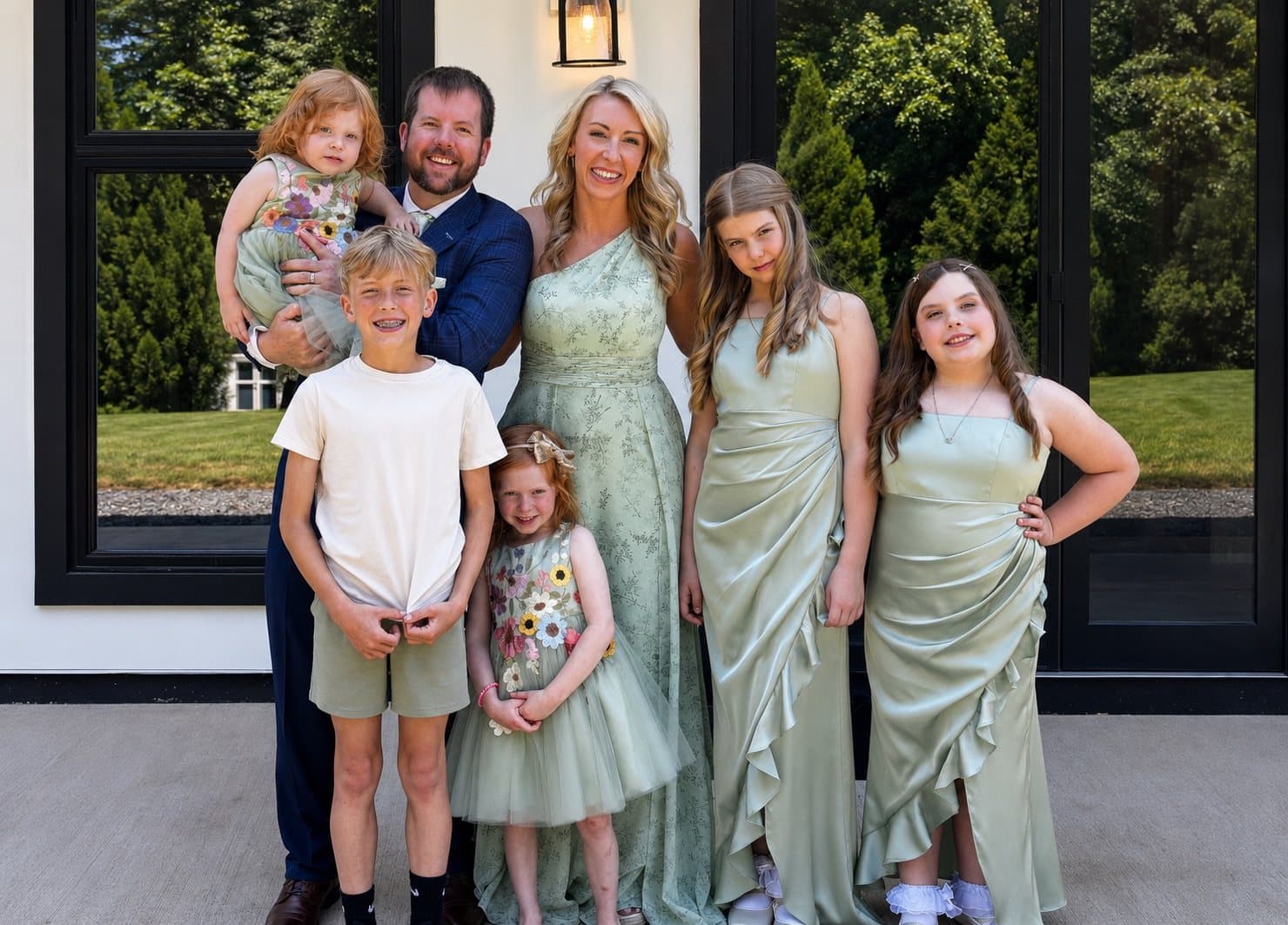 Joe and Julianna Helms with their five children, all dressed in soft green, standing outside a white house.