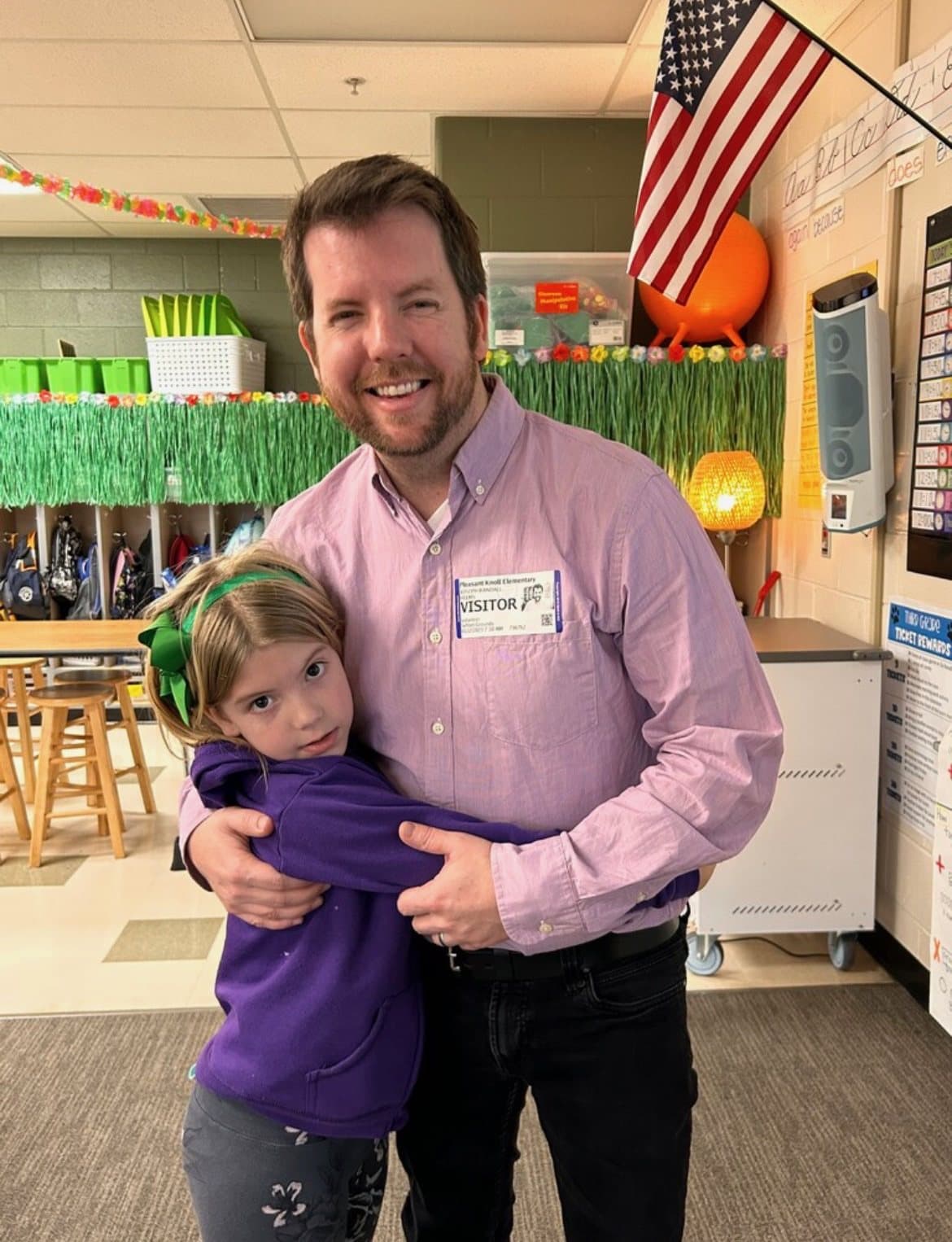 Joe Helms hugging his daughter inside her Fort Mill elementary school classroom while wearing a visitor badge.
