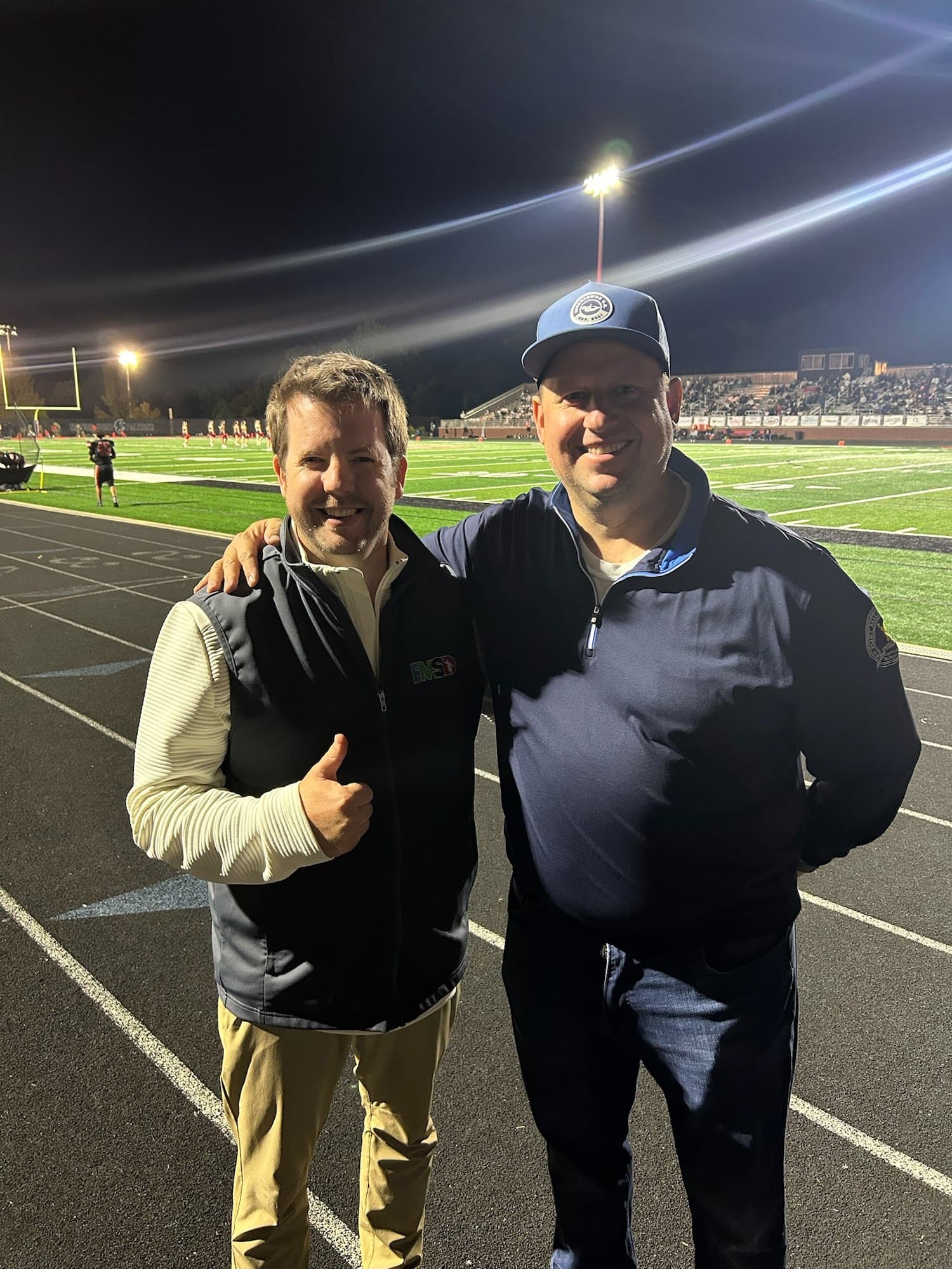 Joe Helms with Grey Young on the track in front of a floodlit Fort Mill football field at night.
