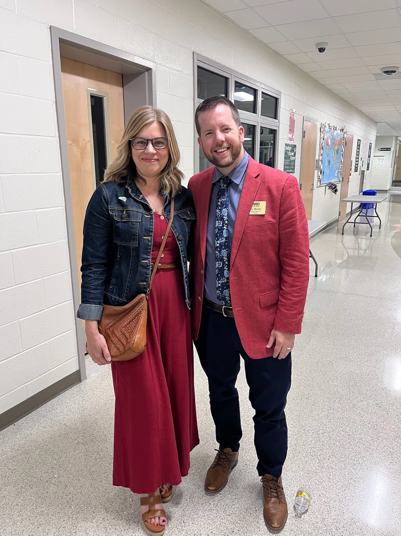 Joe Helms and his wife Julianna standing together in a Fort Mill school hallway. Joe is wearing his school board trustee name badge.