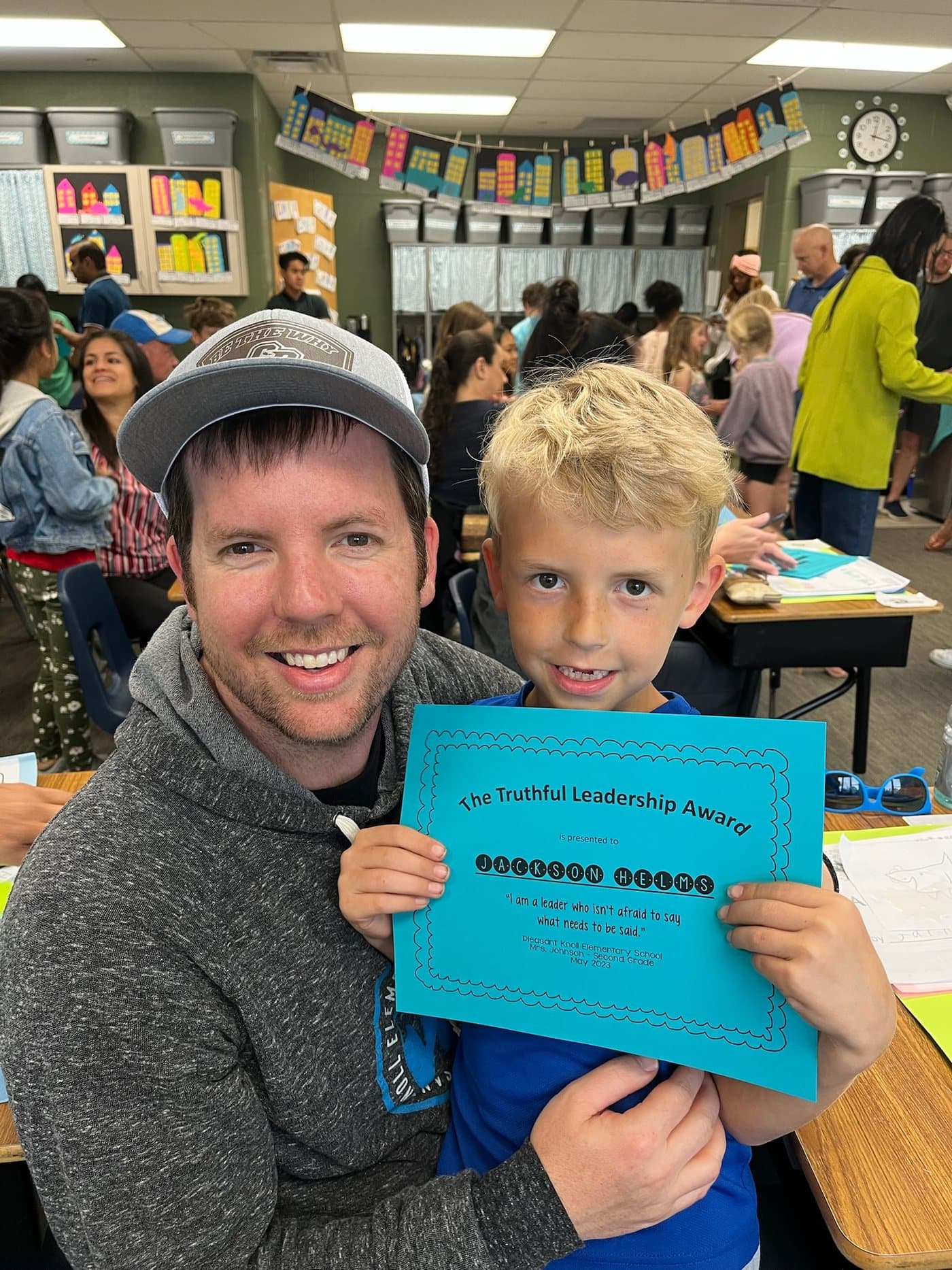 Joe Helms in a school cafeteria with his son, who is holding a certificate awarded by his second grade teacher.